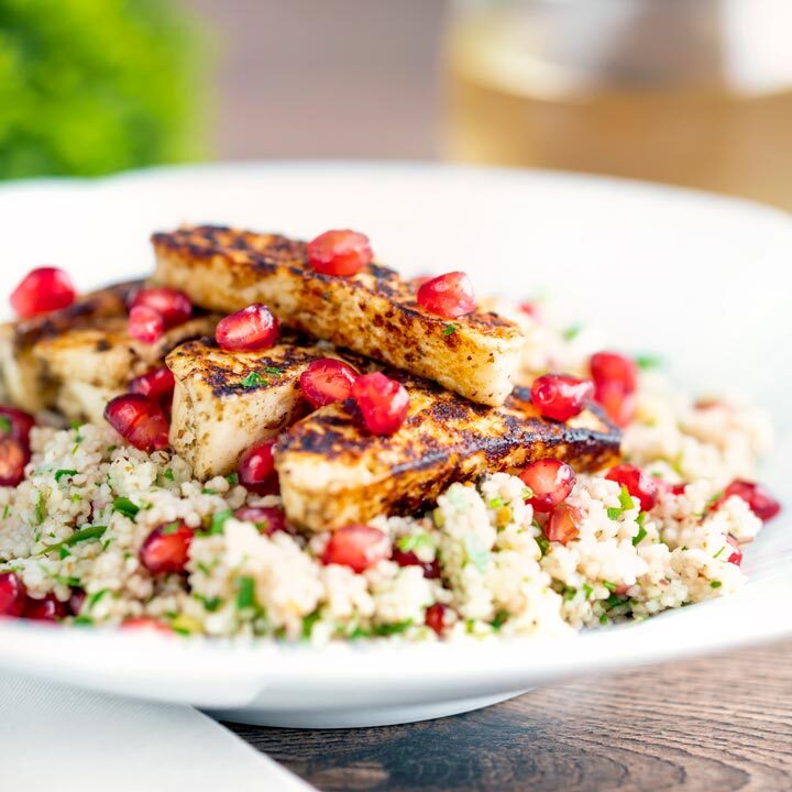 Seared zaatar halloumi cheese salad with pomegranate and couscous served in a white bowl.