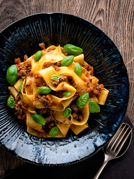 Over head Lamb ragu with pappardelle pasta and fresh basil.