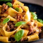 Lamb ragu with pappardelle pasta and fresh basil served on a dark blue plate.