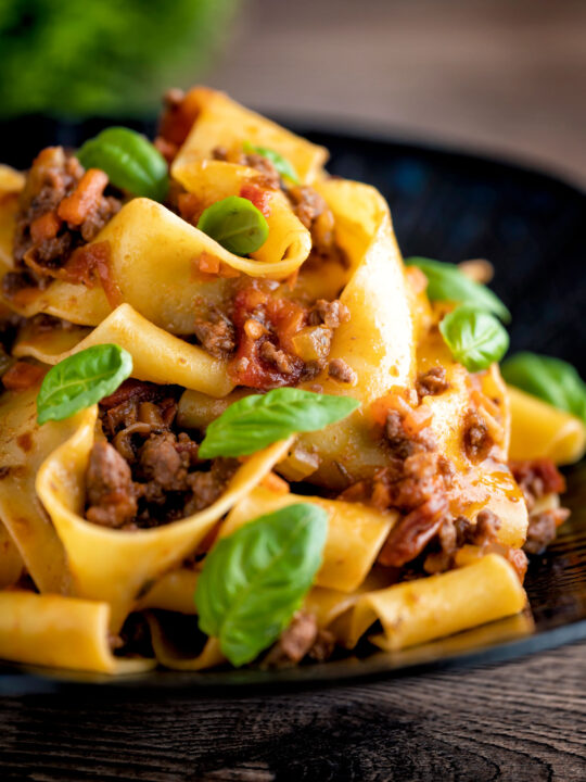 Lamb ragu with pappardelle pasta and fresh basil served on a dark blue plate.