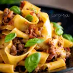 Lamb ragu with pappardelle pasta and fresh basil served on a dark blue plate featuring a title overlay.