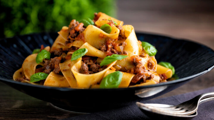 Minced lamb ragu with pappardelle pasta and fresh basil served in a blue plate.