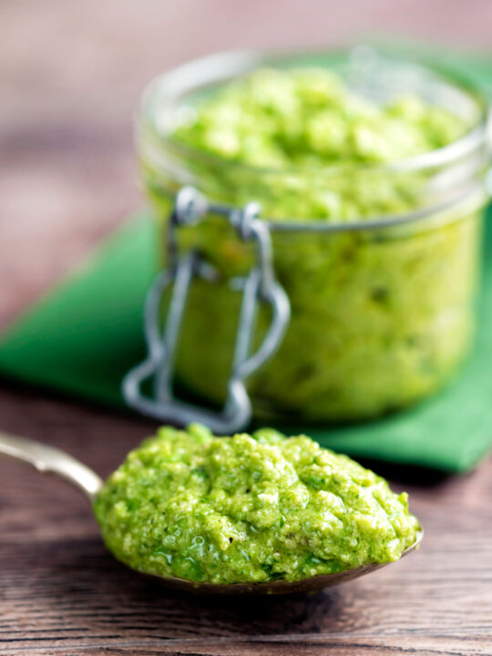 Pea pesto served on a spoon with a jar of pesto in the background.