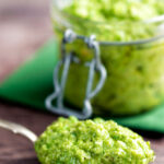 Pea pesto served on a spoon with a jar of pesto in the background featuring a title overlay.