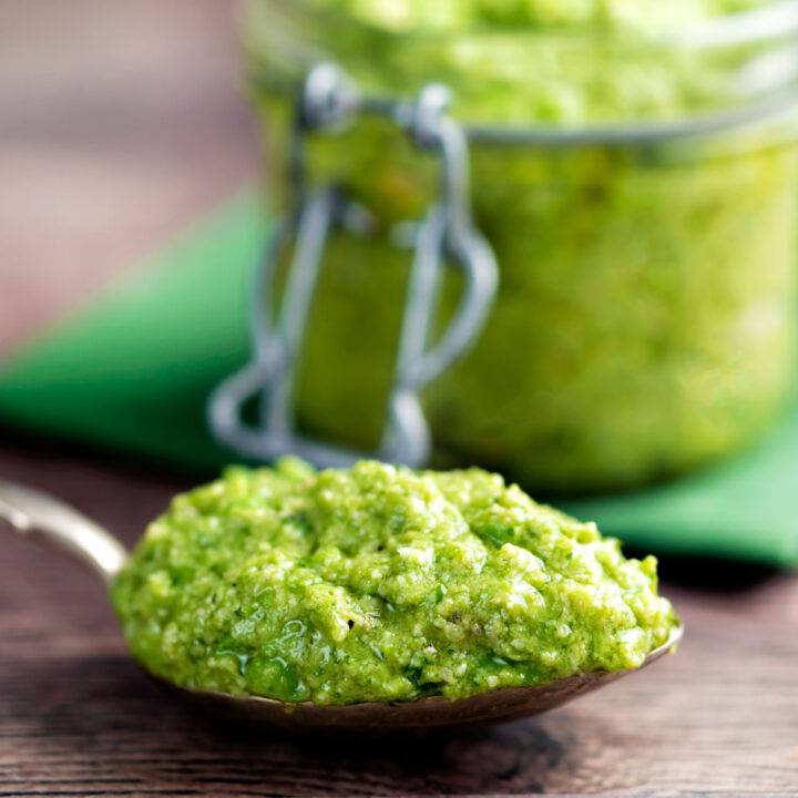 Close up pea pesto on a spoon with a jar of pesto in the background.