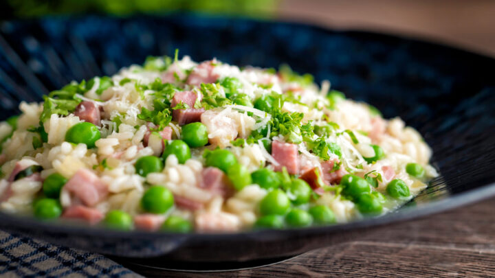 Pea and ham risotto served in a blue bowl garnished with goats cheese and parsley.