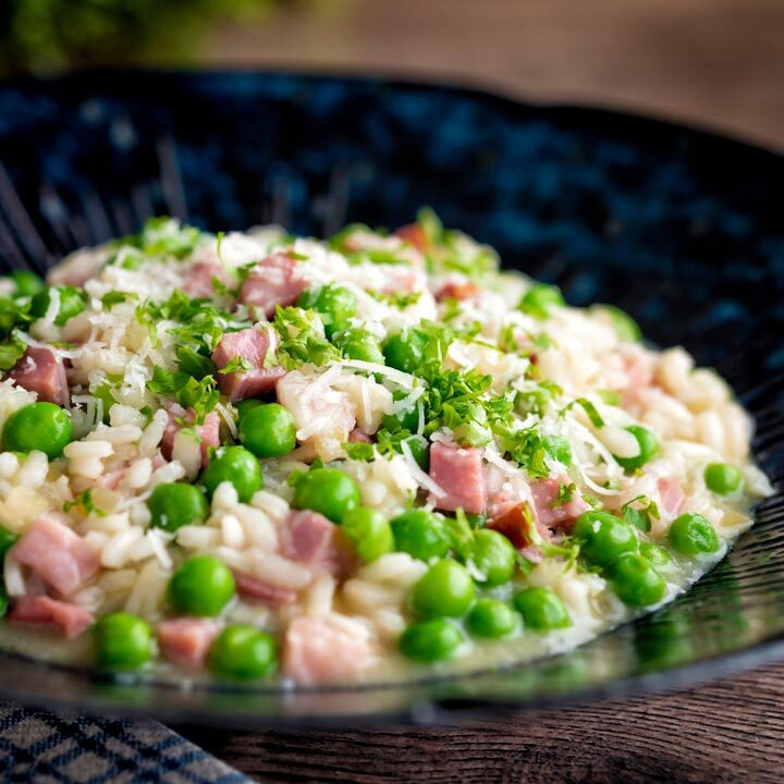 Pea and ham risotto served in a blue bowl.