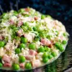 Pea and ham risotto served in a blue bowl garnished with goats cheese and parsley.