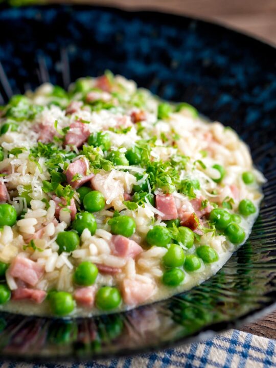 Pea and ham risotto served in a blue bowl garnished with goats cheese and parsley.