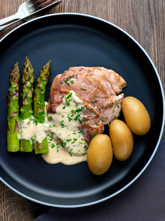 Overhead pork fillet medallions with camembert cheese sauce, potatoes & asparagus.