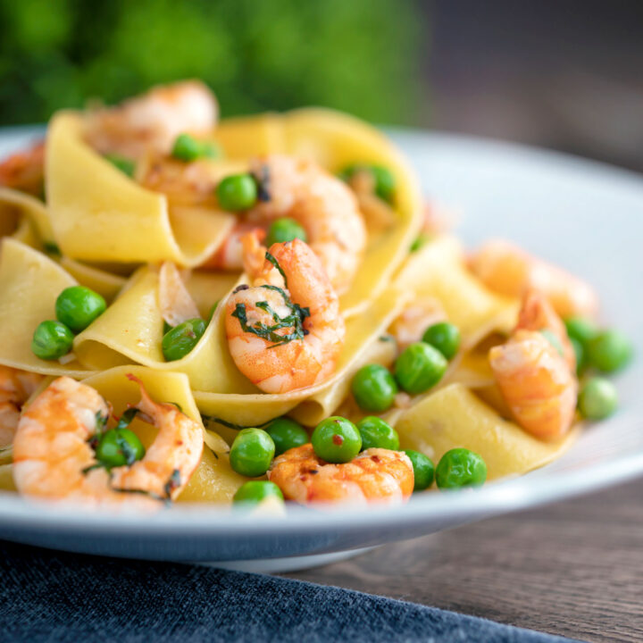 Prawn and pea pasta with pappardelle and chipotle chilli flakes served in a textured bowl.