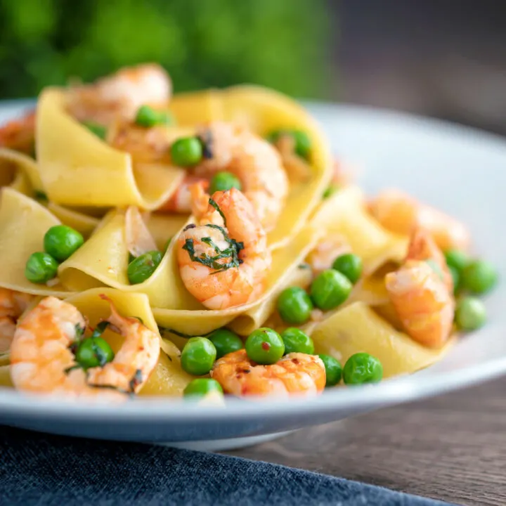 Prawn and pea pasta with pappardelle and chipotle chilli flakes served in a textured bowl.