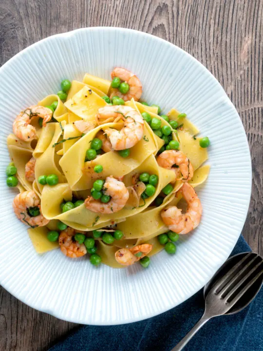 Overhead prawn and pea pasta with pappardelle served in a textured bowl.