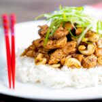 Szechuan chicken with cashew nuts served with white rice featuring red chopsticks.
