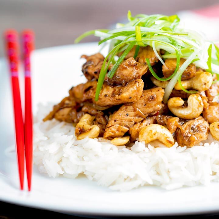 Szechuan chicken with cashew nuts served with white rice featuring red chopsticks.