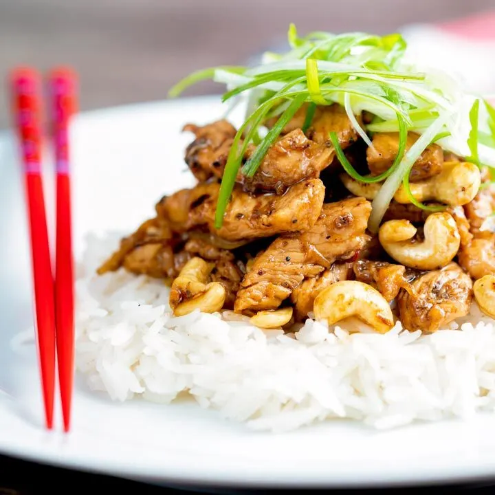 Szechuan chicken with cashew nuts served with white rice featuring red chopsticks.