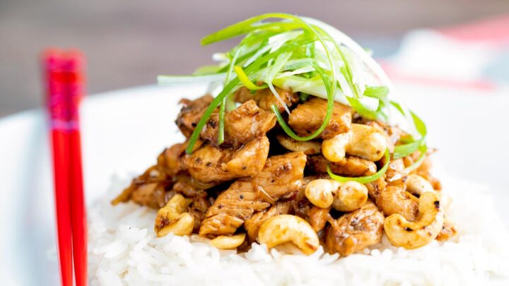 Szechuan chicken with cashew nuts served with white rice & shredded green onion featuring red chopsticks.