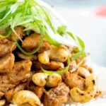 Close up Szechuan chicken with cashew nuts and spring onion served on white rice.