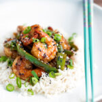 Szechuan prawns with green pepper served on steamed rice in a white bowl.