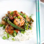 Szechuan prawns with green pepper served on steamed rice in a white bowl.