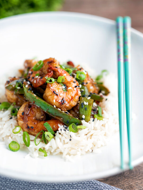 Szechuan prawns with green pepper served on steamed rice in a white bowl.