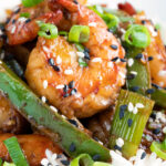 Close up Szechuan prawns with green pepper served on steamed rice in a white bowl.
