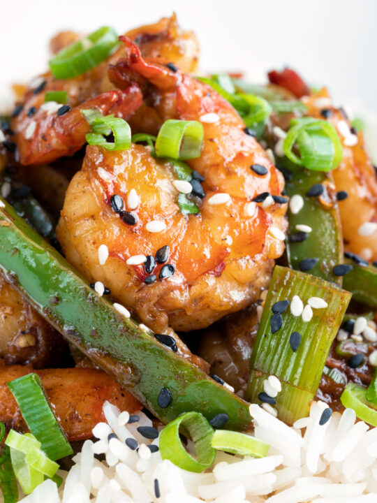 Close up Szechuan prawns with green pepper served on steamed rice in a white bowl.