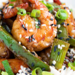 Close up Szechuan prawns with green pepper served on steamed rice in a white bowl featuring a title overlay.