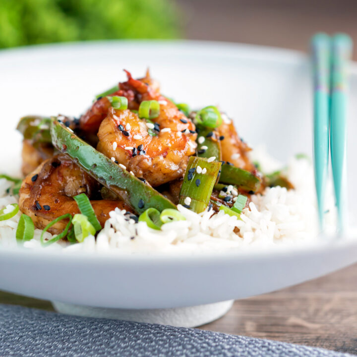 Spicy Szechuan prawns with green pepper served on steamed rice in a white bowl.