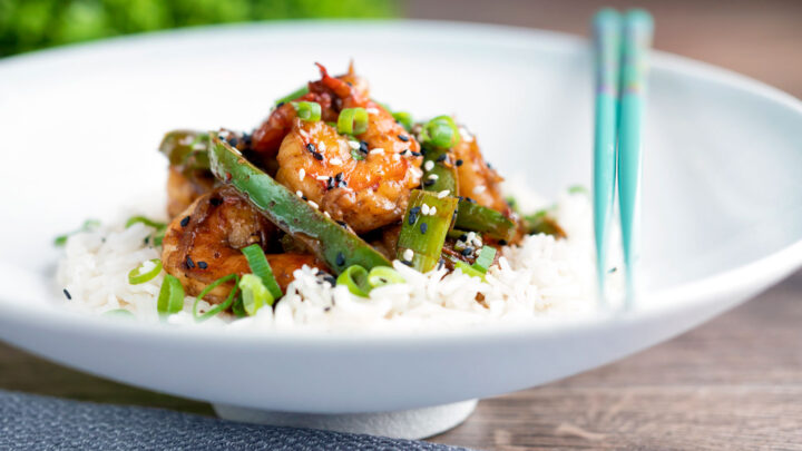 Szechuan prawns stir fry with green pepper served on steamed rice in a white bowl.