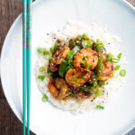 Overhead Szechuan prawns with green pepper served on steamed rice in a white bowl.