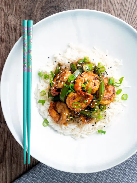 Overhead Szechuan prawns with green pepper served on steamed rice in a white bowl.