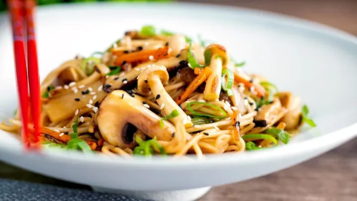 Stir fried vegetarian mushroom chow mein noodles served in a white bowl with red chopsticks.