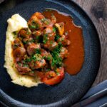 Overhead wild boar stew with mushrooms served with mashed potato on a dark plate.