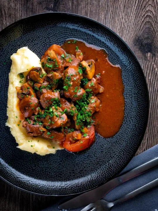 Overhead wild boar stew with mushrooms served with mashed potato on a dark plate.