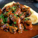 Wild boar stew with mushrooms served with mashed potato on a dark plate featuring a title overlay.