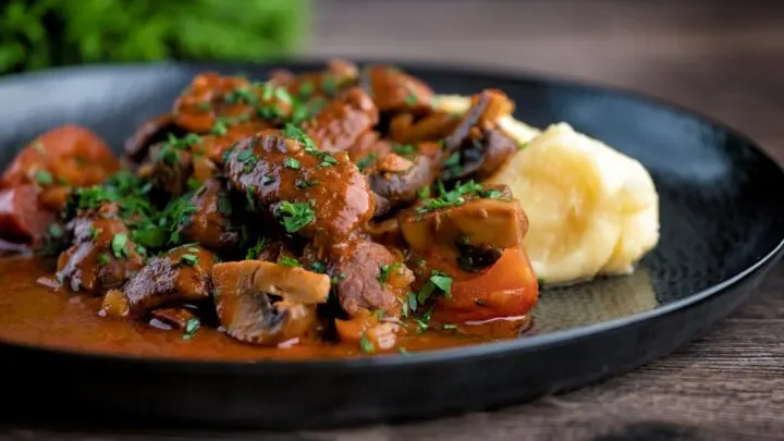 Wild boar stew with mushrooms served with mashed potato and a parsley garnish.