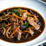 Beef noodle soup featuring udon noodles, spinach & carrot in a dark soy broth.