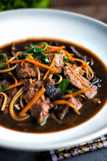 Beef noodle soup featuring udon noodles, spinach & carrot in a dark soy broth.