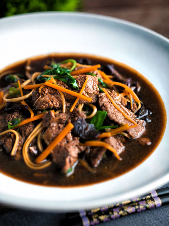 Beef noodle soup featuring udon noodles, spinach & carrot in a dark soy broth.