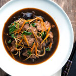 Overhead beef noodle soup featuring udon noodles & spinach in a dark soy broth