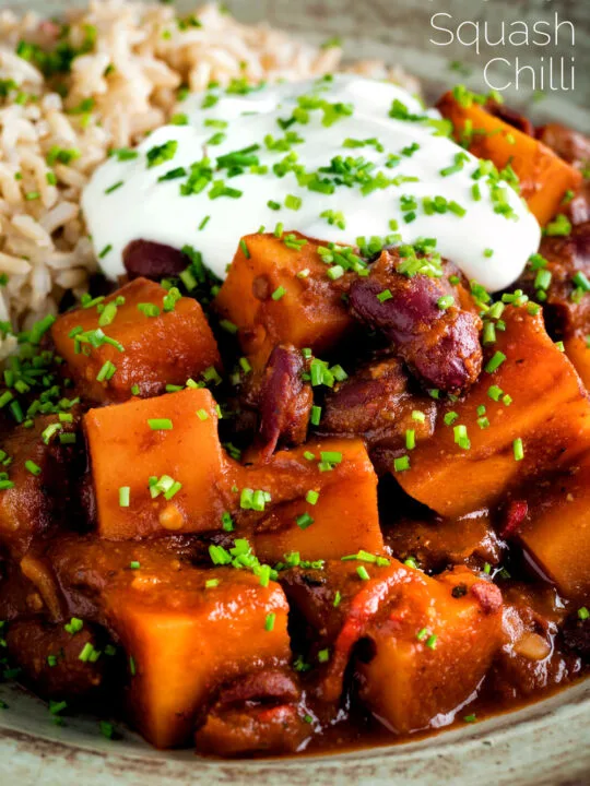 Close up butternut squash chilli served with brown rice, and sour cream featuring a title overlay.