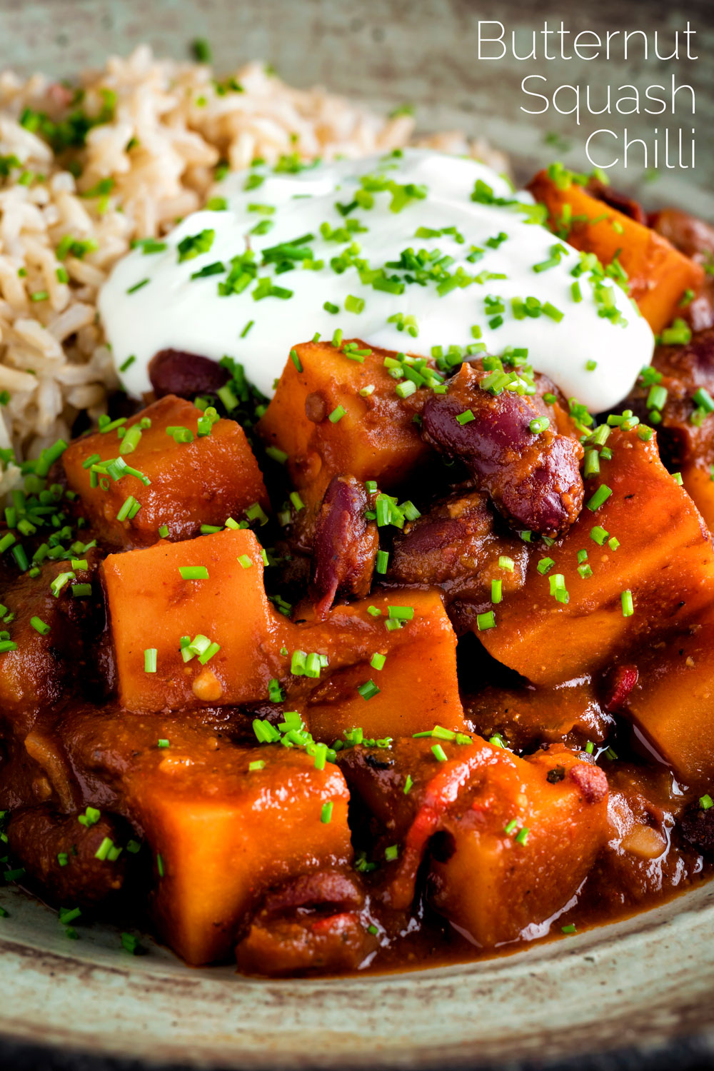 Close up butternut squash chilli served with brown rice, and sour cream featuring a title overlay.
