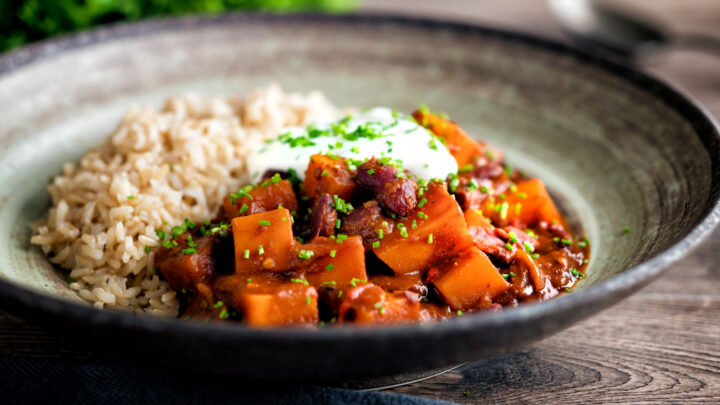 Butternut squash chilli served with brown rice, and sour cream in an earthenware bowl.