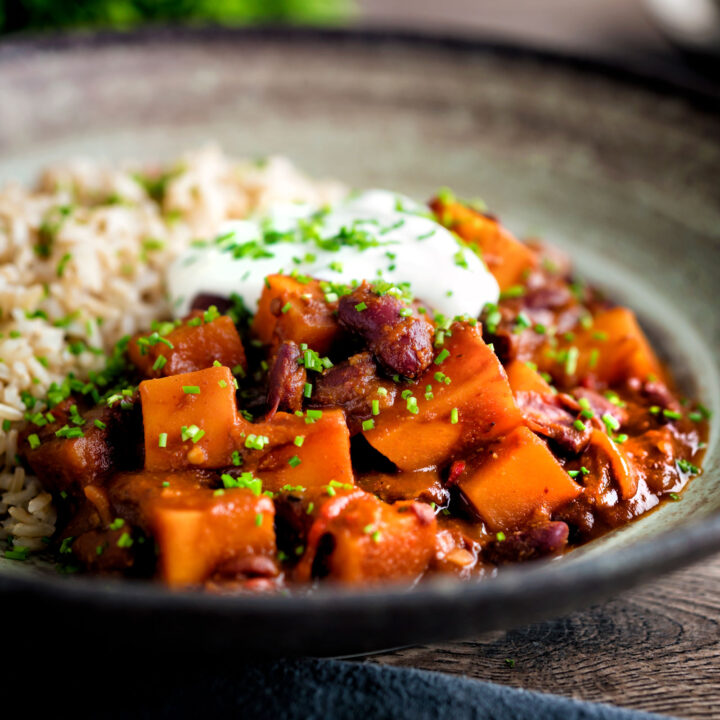 Butternut squash chilli served with brown rice, and sour cream in an earthenware bowl.