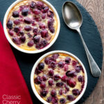 Overhead individual cherry clafoutis desserts served in brulée pots featuring a title overlay.