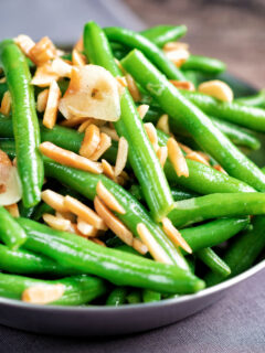 Close up garlic green beans served in a small pan garnished with almonds.