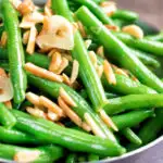 Close up garlic green beans served in a small pan garnished with almonds featuring a title overlay.