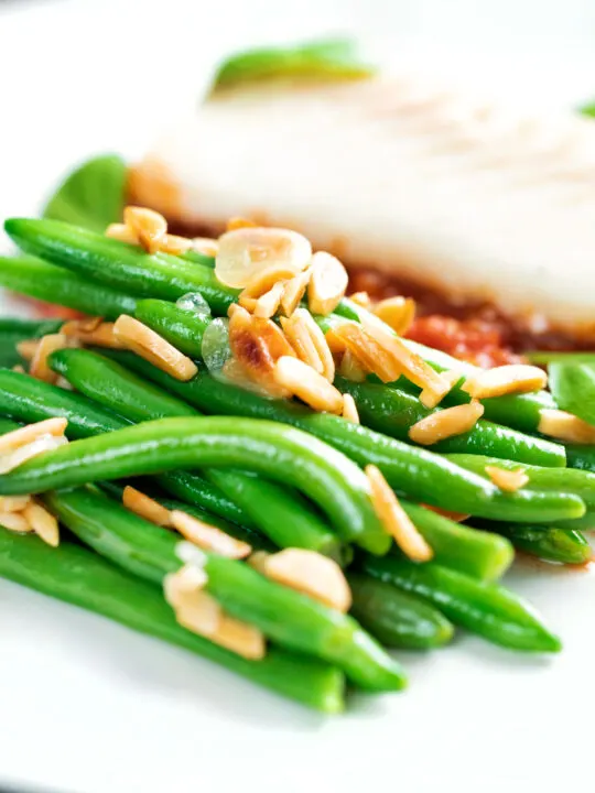 Garlic green beans served on a white plate garnished with almonds.