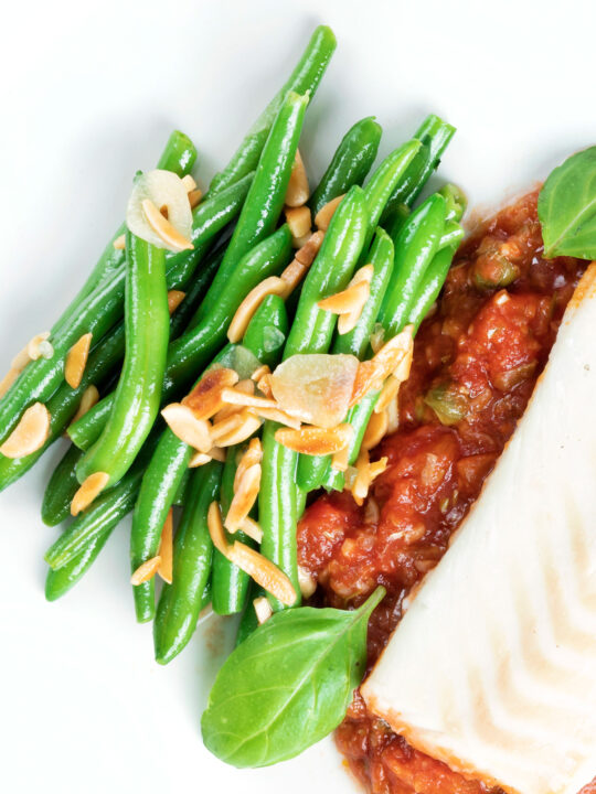 Overhead garlic green beans served on a white plate garnished with almonds.